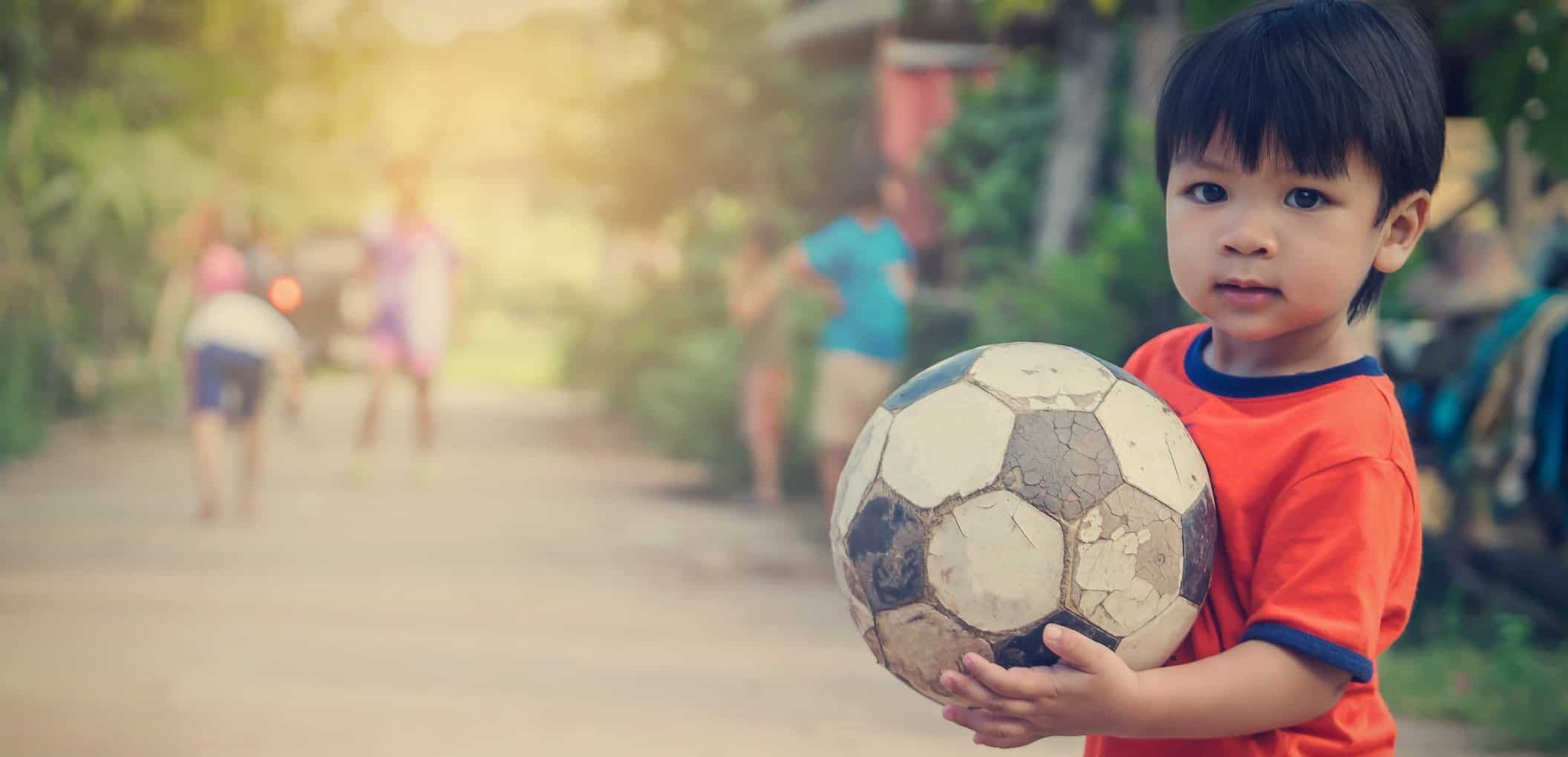 Asian Boy Playing With Old Rustic Soccer Ball