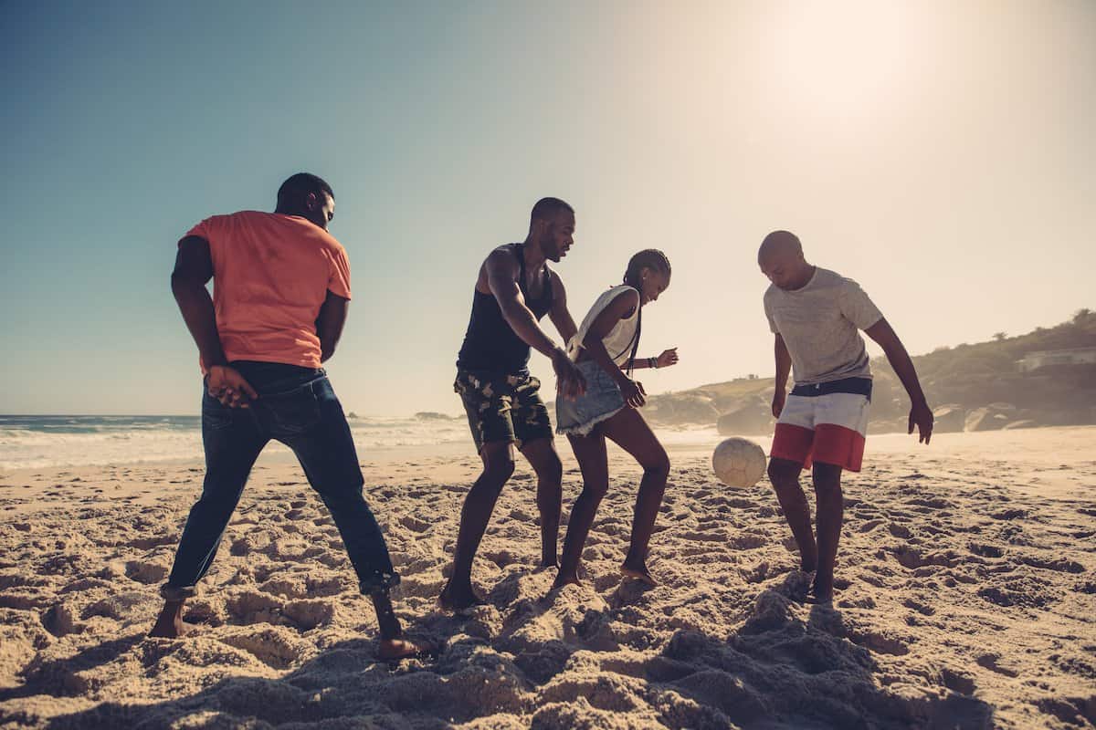 Friends Enjoying A Game Of Soccer At Beach